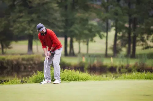 A man in red shirt playing golf on green.